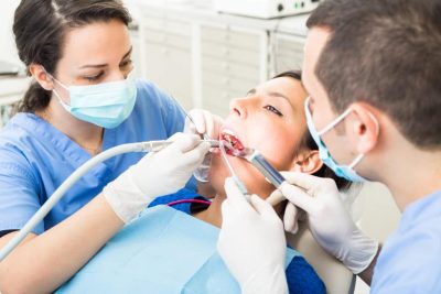 Dentist and dental assistant examining patient teeth. Dentist and Patient are Women, Assistant is a Man. Patient is Relaxed and not scared of Dentist.